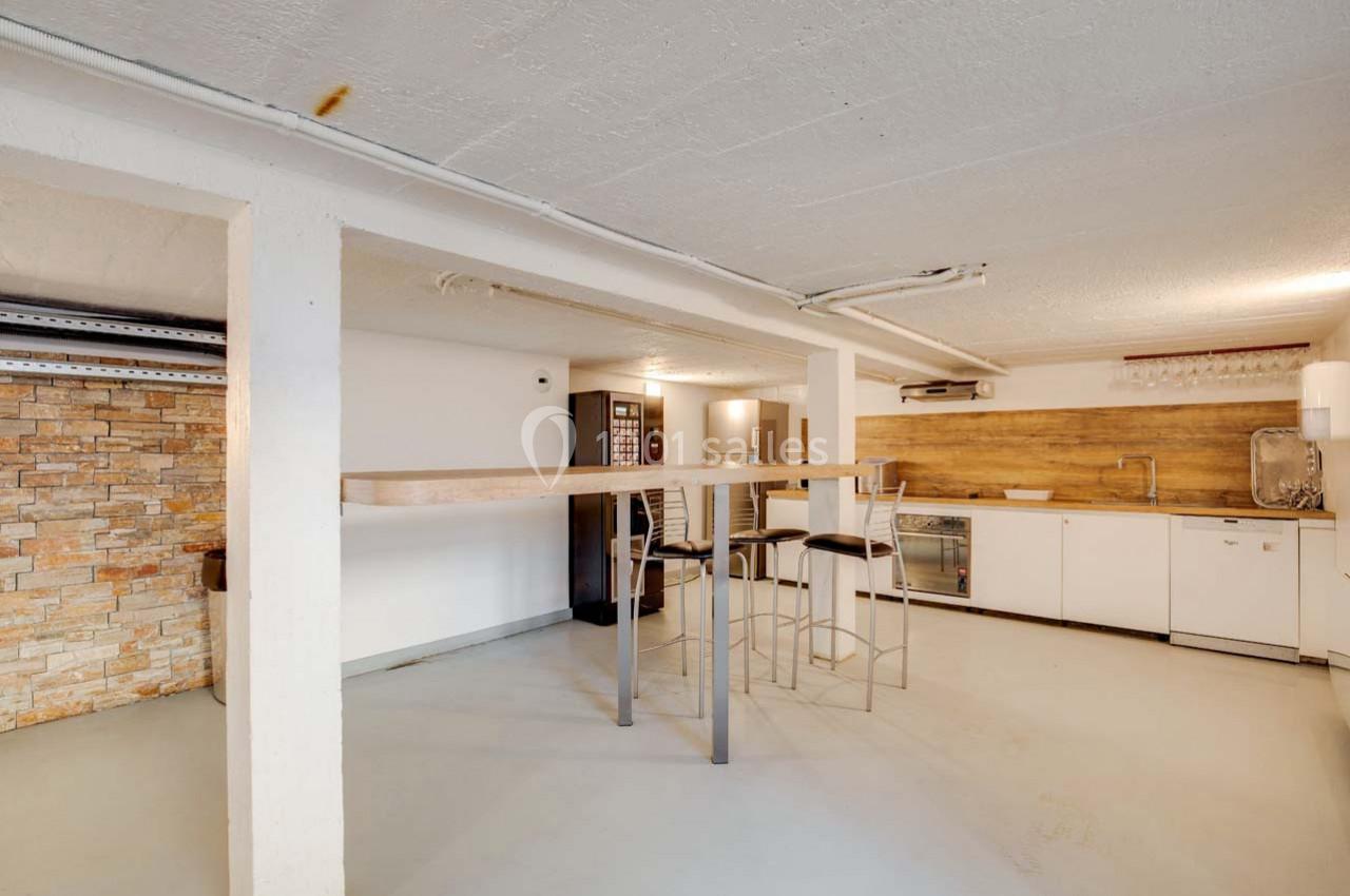 Espace intérieur avec un comptoir haut, tabourets, cuisine équipée et mur en pierre apparente.