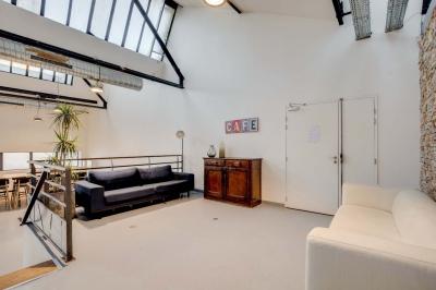 Salle lumineuse avec rangées de chaises, tables hautes et buffet en arrière-plan, sous un plafond industriel.