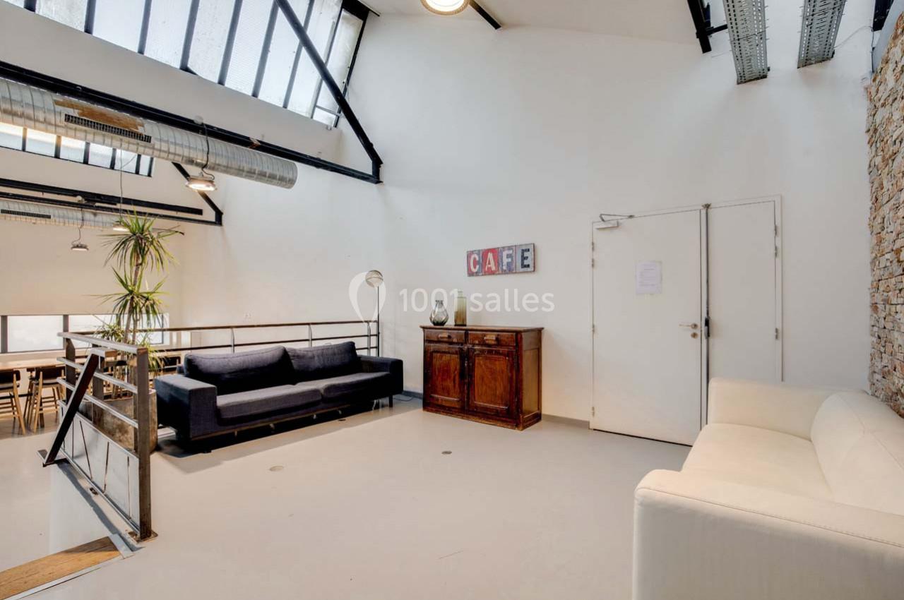 Espace lumineux avec canapé, fauteuil, meuble en bois et mur en briques, sous une verrière inclinée.