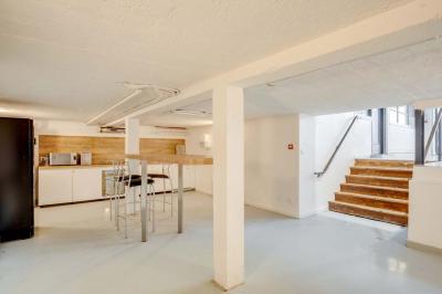 Salle lumineuse avec rangées de chaises, tables hautes et buffet en arrière-plan, sous un plafond industriel.