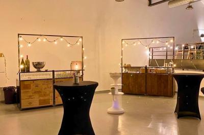 Salle lumineuse avec rangées de chaises, tables hautes et buffet en arrière-plan, sous un plafond industriel.