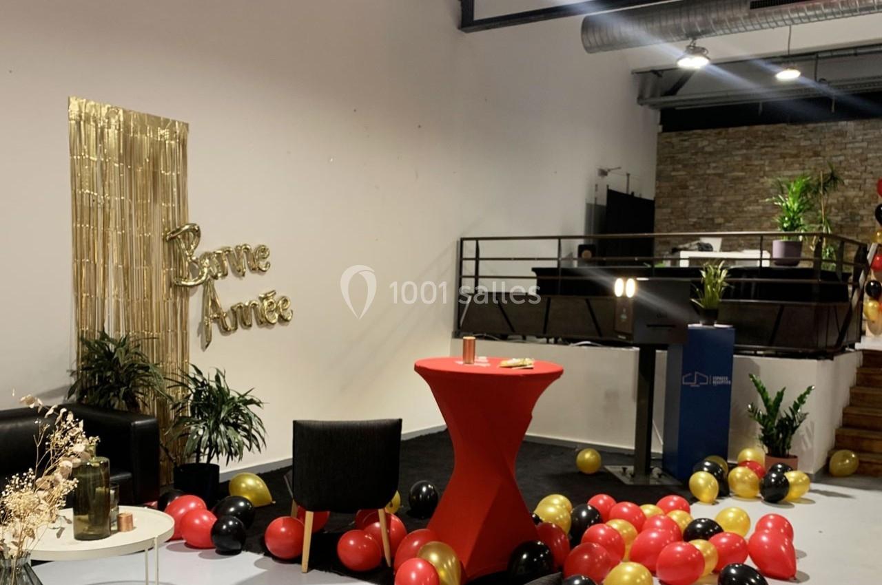 Salle décorée pour le Nouvel An avec ballons rouges, noirs et dorés, table haute rouge et panneau ’Bonne Année’.
