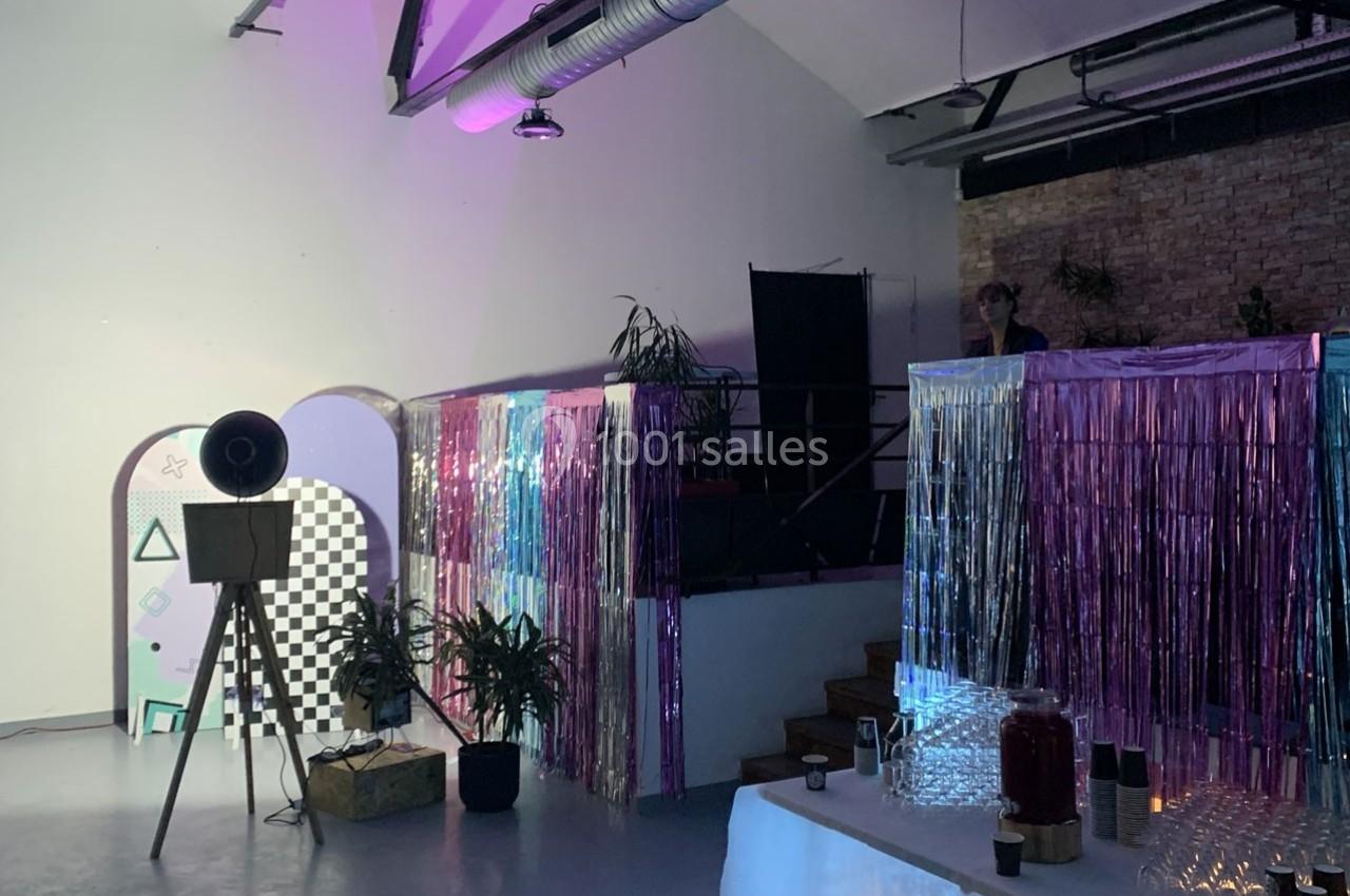 Salle décorée avec des rideaux métallisés colorés, un projecteur rétro, des plantes et une table avec boissons.