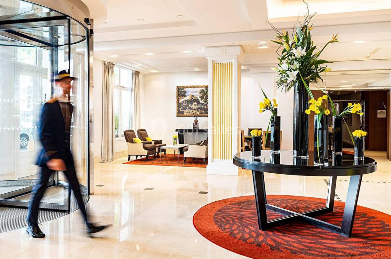 Hall d'entrée lumineux avec un tapis rouge, une table décorée de fleurs et un portier en mouvement.