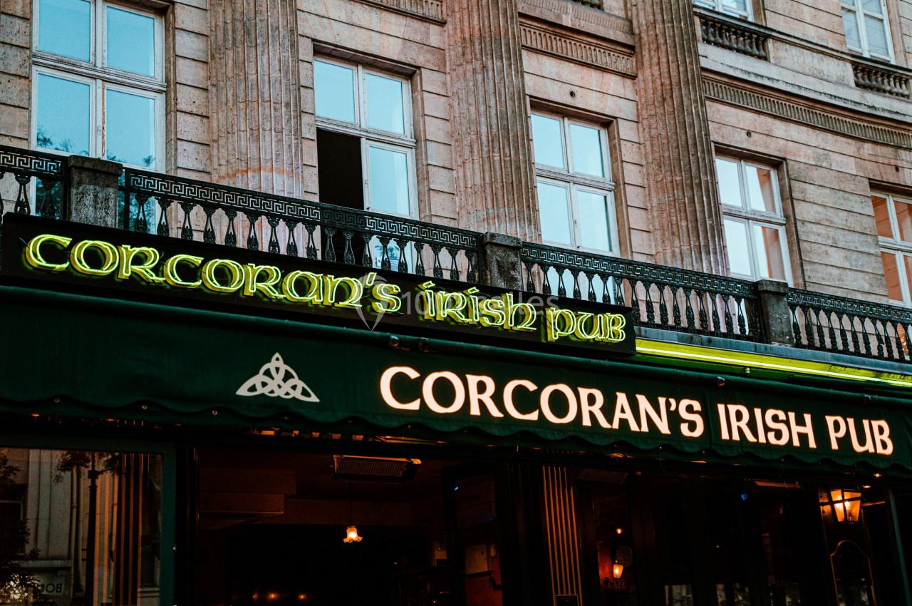 Façade d'un pub irlandais avec enseignes lumineuses vertes et jaunes, devant un bâtiment en pierre.