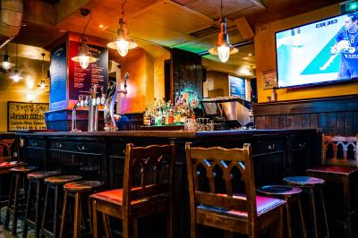 Façade d'un pub irlandais avec enseignes lumineuses vertes et jaunes, devant un bâtiment en pierre.