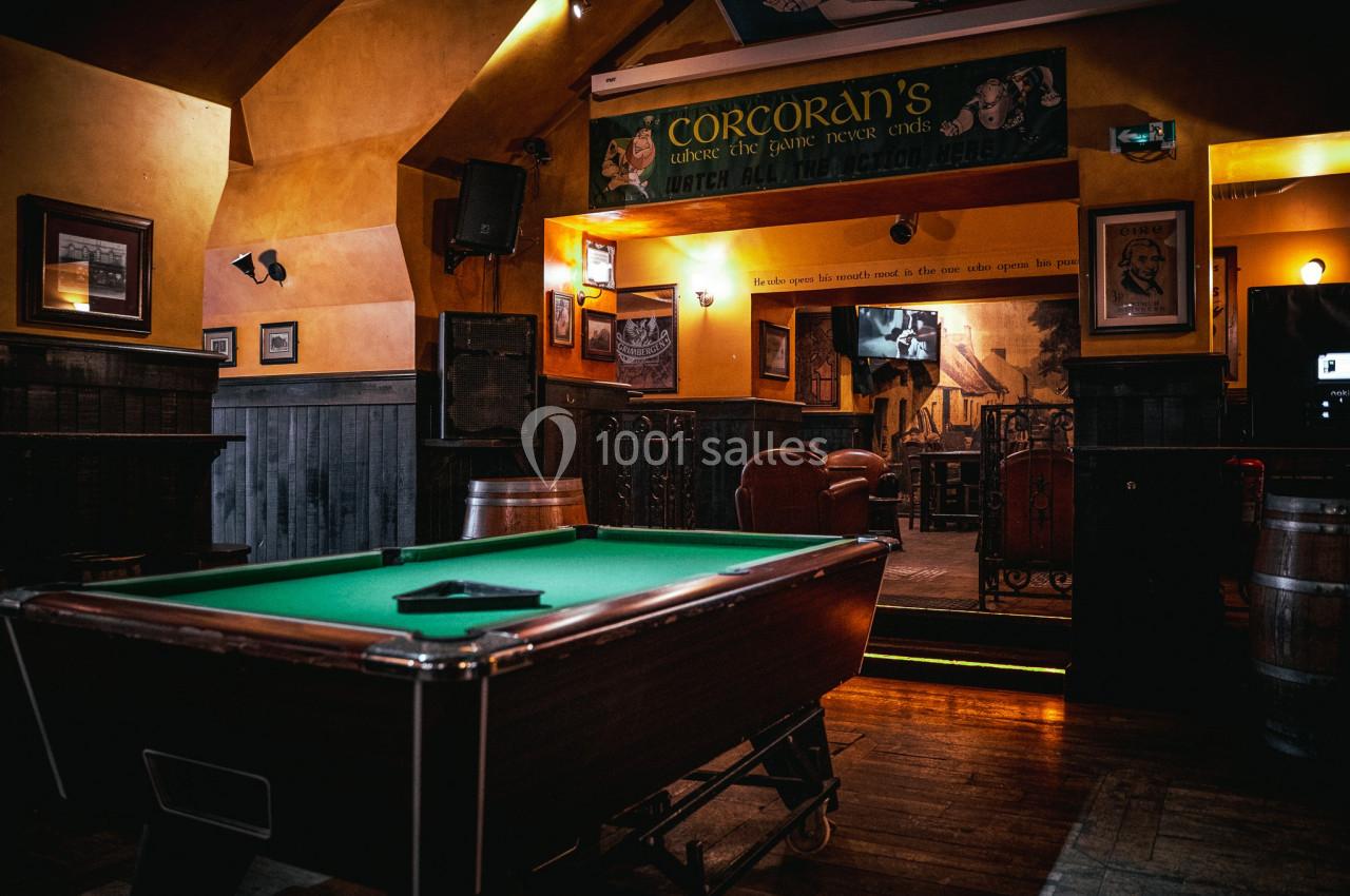 Table de billard dans un bar à l'ambiance chaleureuse avec éclairage tamisé et décorations murales.