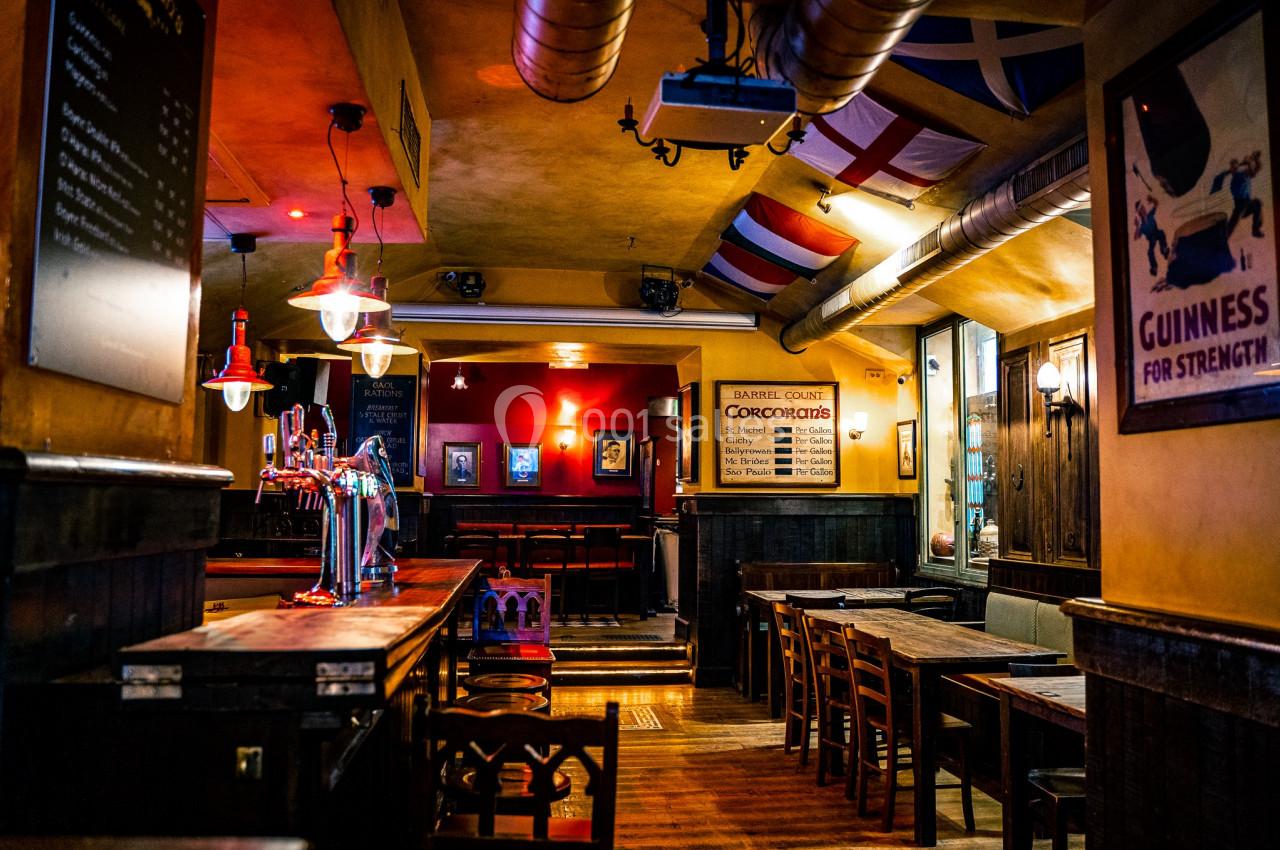 Intérieur d'un pub chaleureux avec des tables en bois, un bar éclairé et des drapeaux suspendus au plafond.