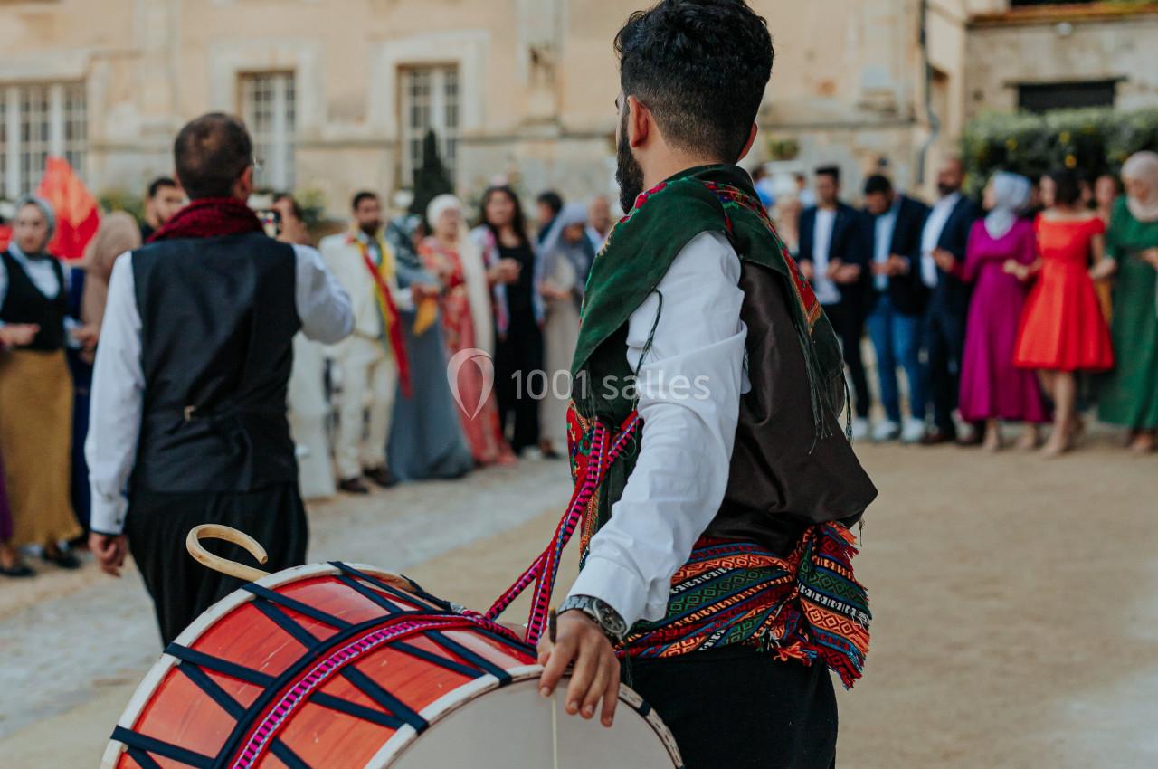 Un musicien joue du tambour devant un groupe de personnes rassemblées près d'un bâtiment ancien.