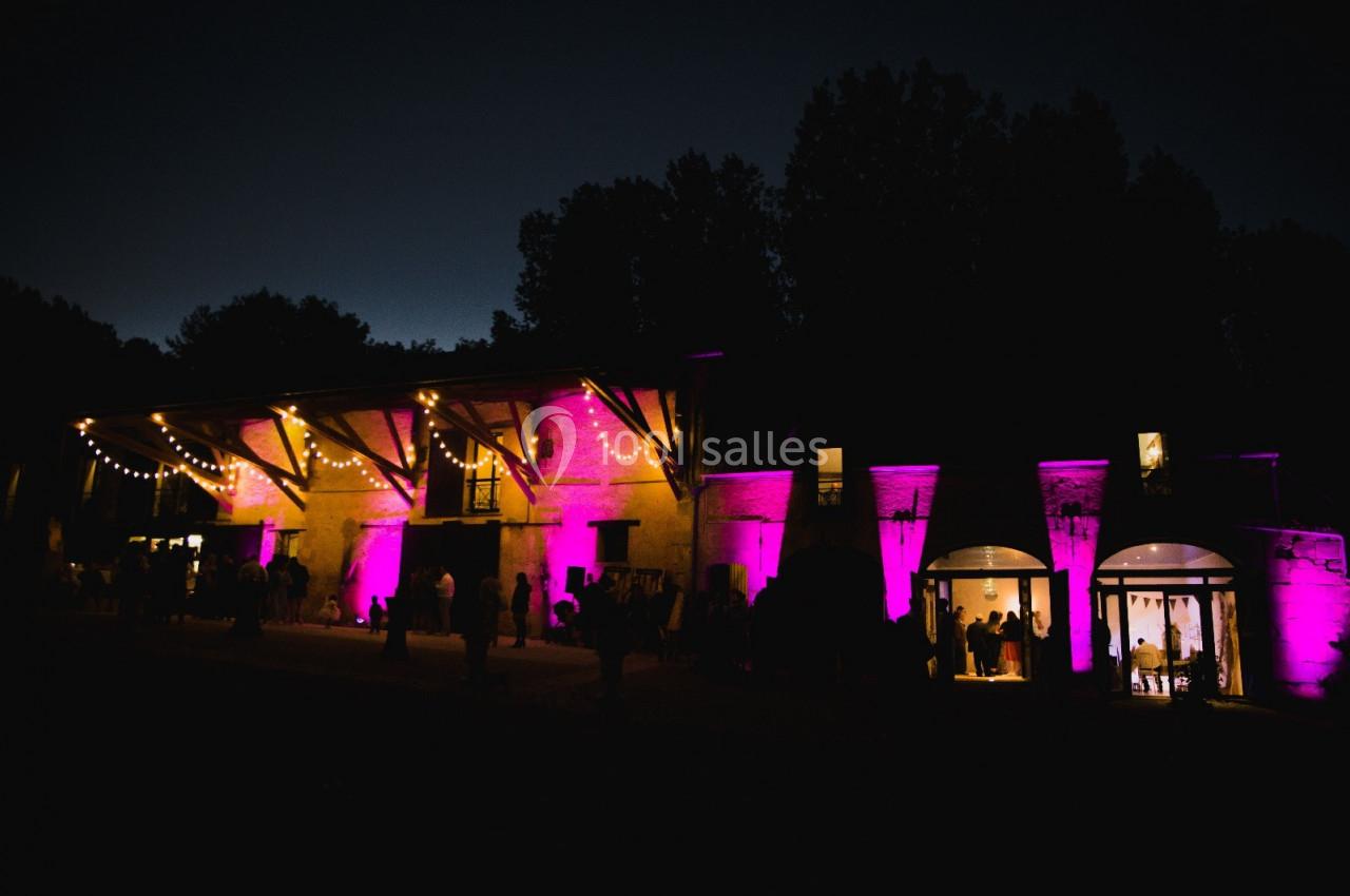 Bâtiment éclairé par des lumières violettes et guirlandes lumineuses, avec des silhouettes de personnes à l'extérieur, de…