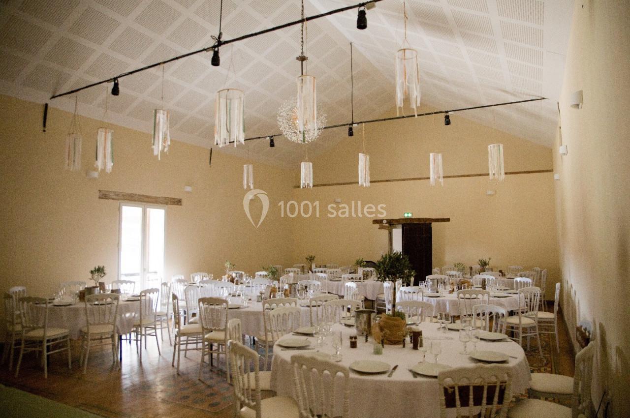 Salle de réception lumineuse avec des tables rondes dressées, des chaises blanches et des suspensions décoratives.