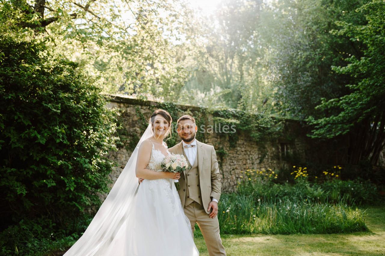 Un couple en tenue de mariage pose dans un jardin verdoyant sous une lumière naturelle.
