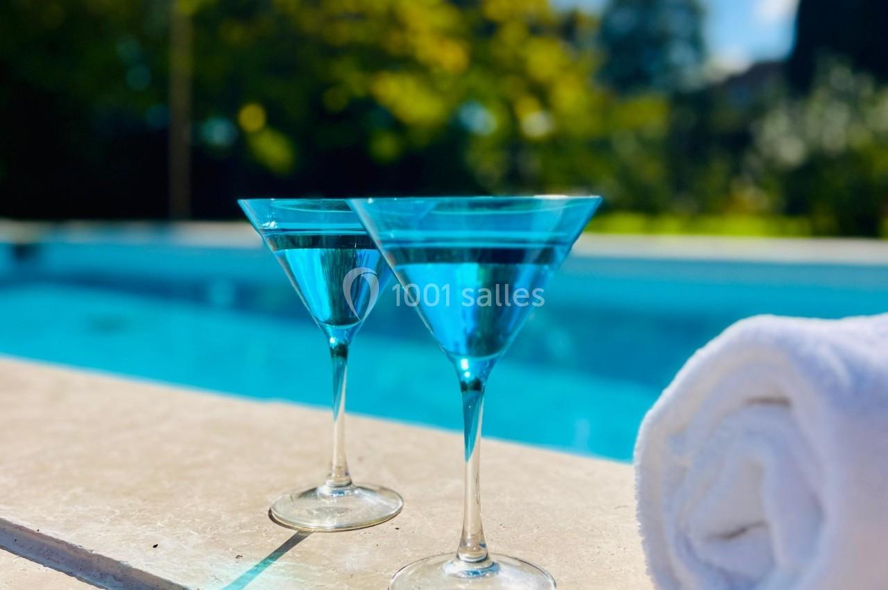 Deux verres de cocktail bleu posés sur le bord d'une piscine, avec une serviette blanche enroulée à côté.
