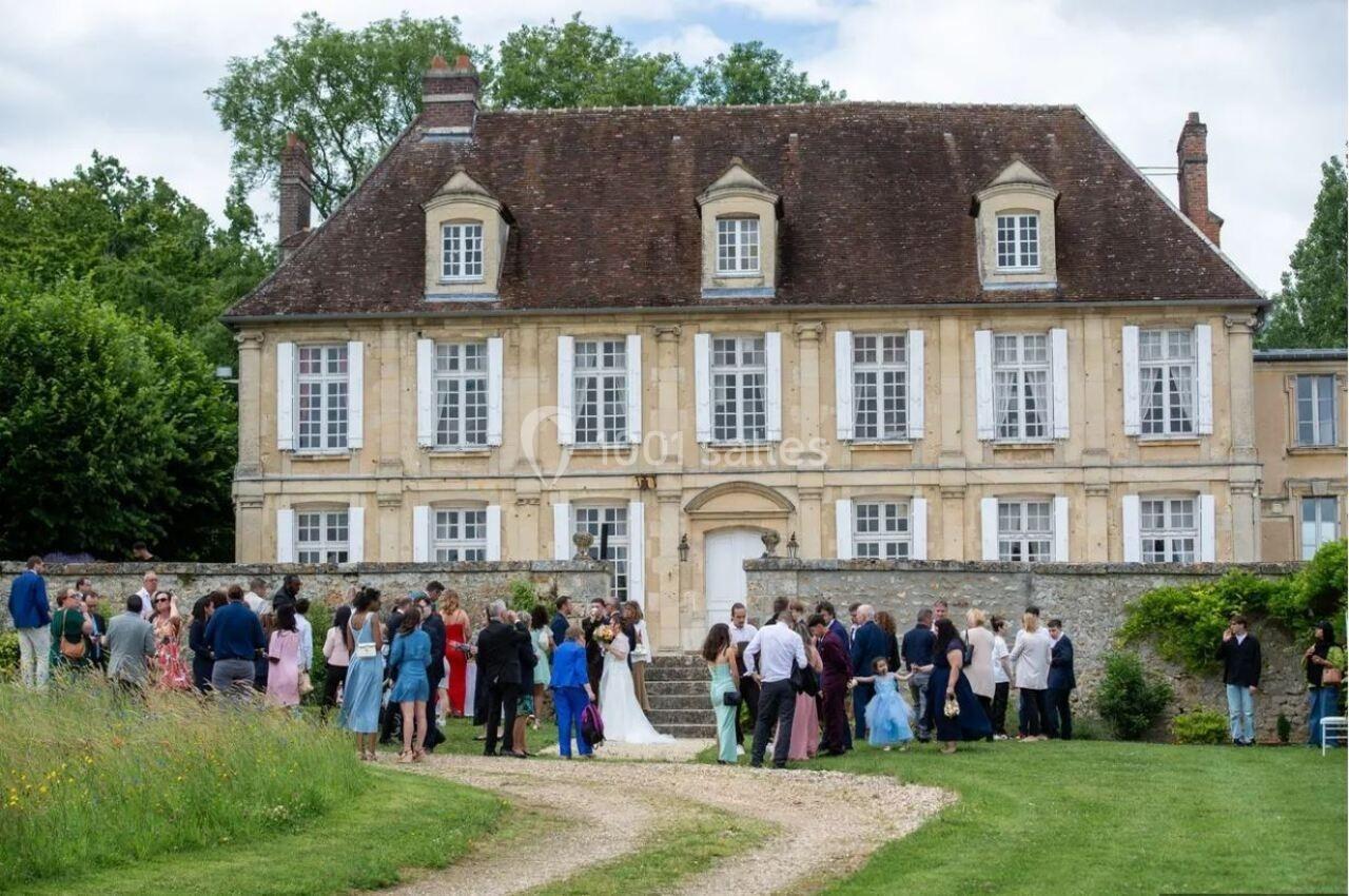 Groupe de personnes rassemblées devant un grand bâtiment ancien en pierre, entouré de verdure.