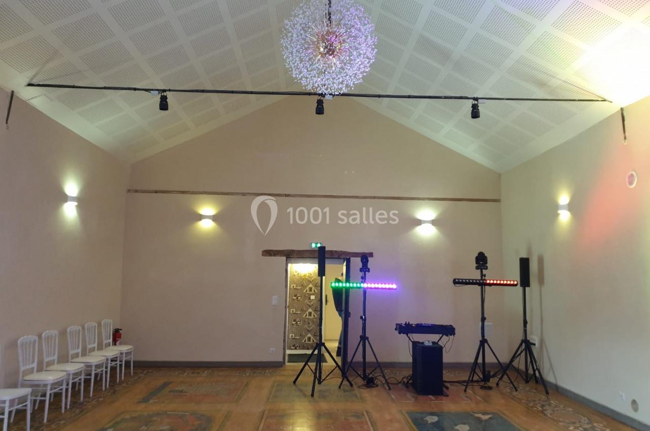 Salle lumineuse avec plafond haut, chaises alignées à gauche, équipements d'éclairage et de son installés au fond.