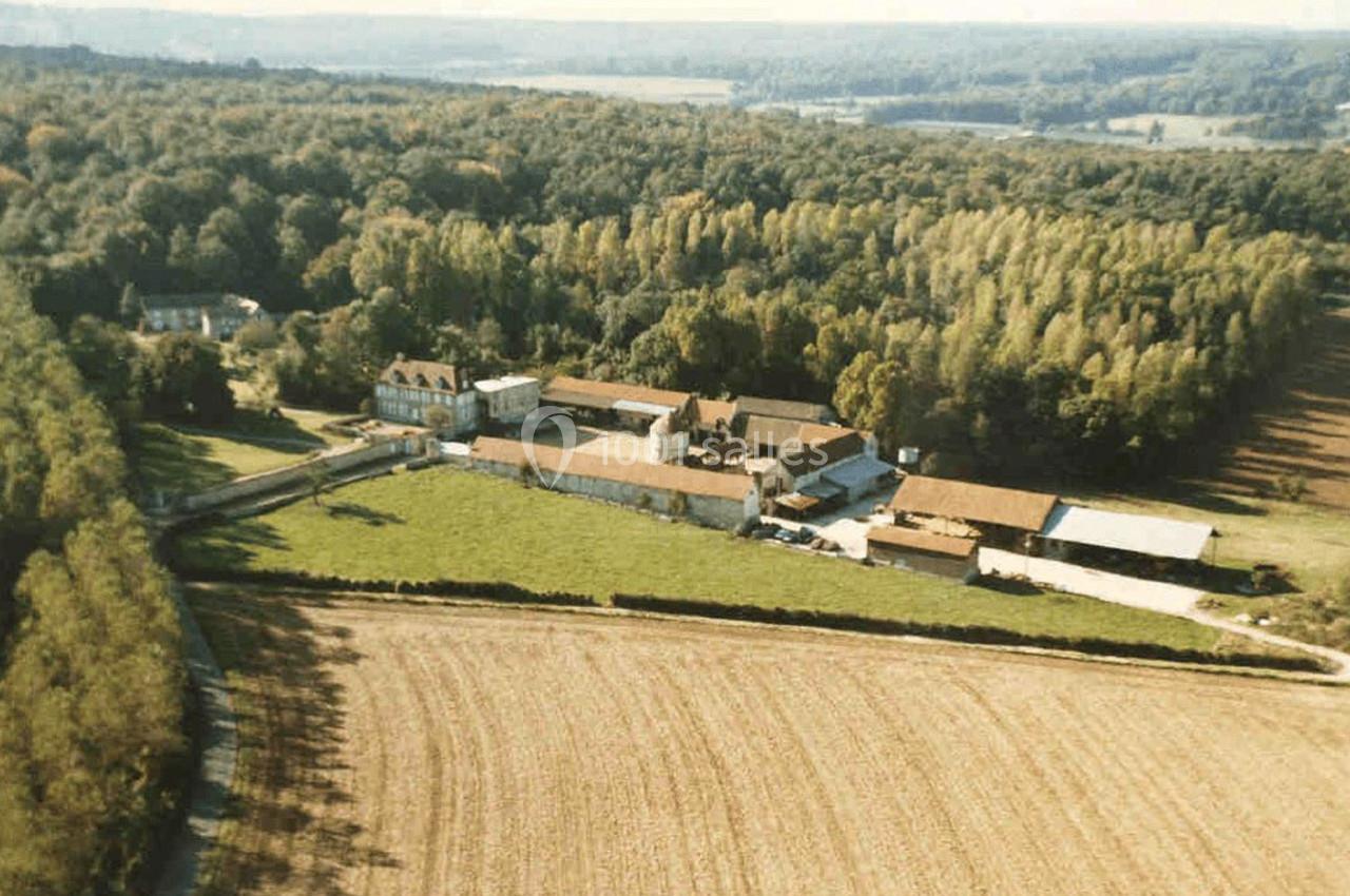 Vue aérienne d'un domaine rural entouré de champs et de forêts, avec plusieurs bâtiments en pierre et toits en tuiles.
