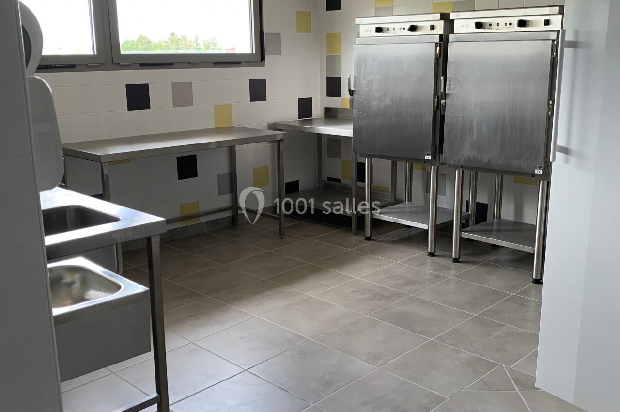 Cuisine professionnelle avec éviers en inox, plans de travail, carrelage au sol et murs ornés de carreaux colorés.