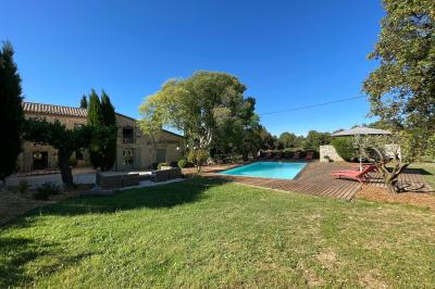 Cour d'une maison en pierre éclairée la nuit, avec arbres, mobilier de jardin et chemin bordé de lampes.