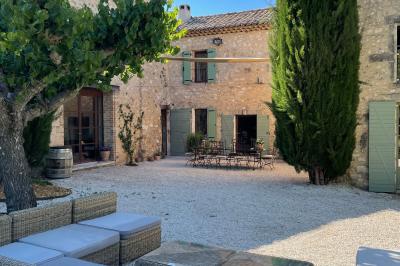 Cour d'une maison en pierre éclairée la nuit, avec arbres, mobilier de jardin et chemin bordé de lampes.