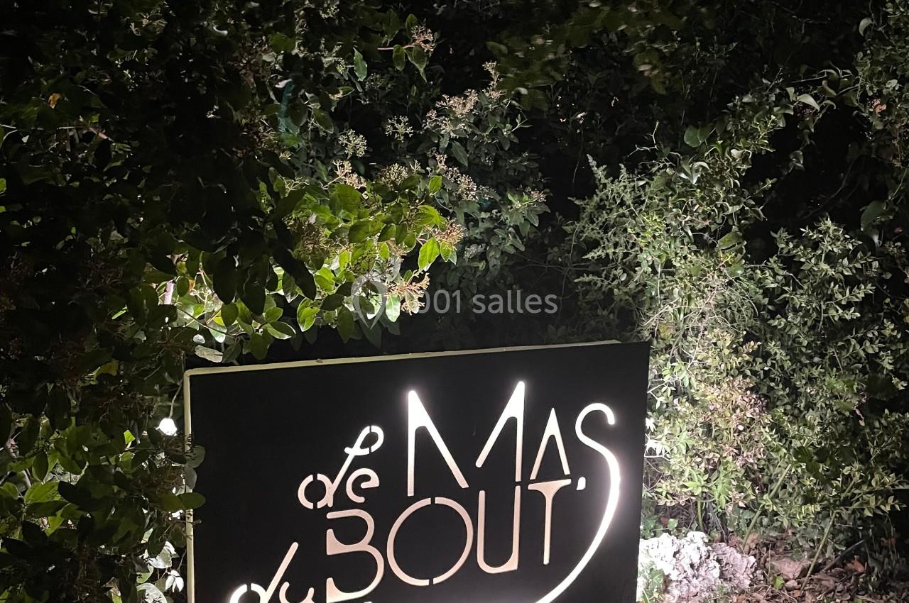 Panneau lumineux ’Le Mas du Bout’ entouré de végétation, photographié de nuit.