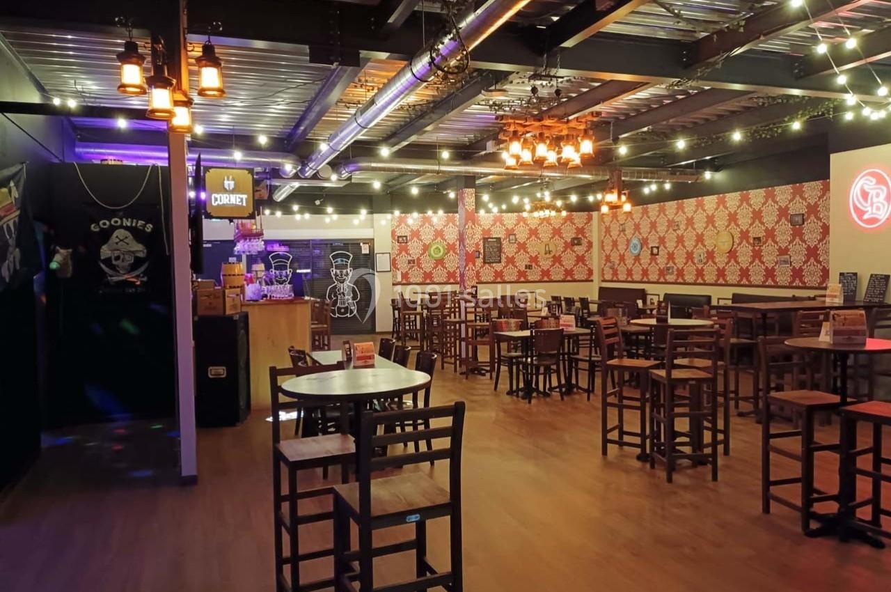 Salle de restaurant avec tables en bois, décorations murales rouges et lumières suspendues dans une ambiance chaleureuse.