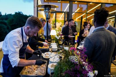 Quatre personnes regardent un coucher de soleil aux teintes orange et violet depuis une terrasse surplombant des vignes.