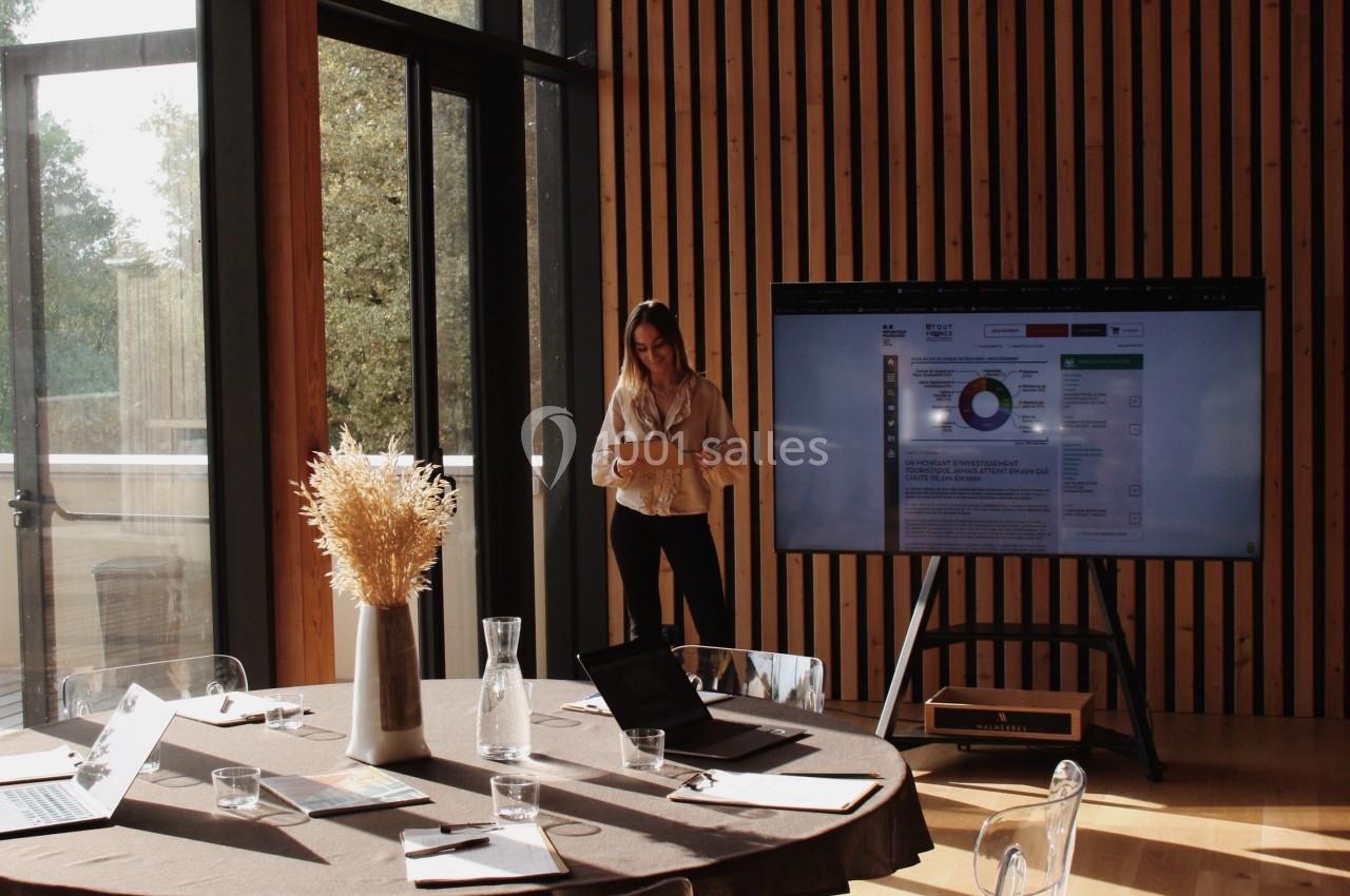 Une femme se tient près d'un écran de présentation dans une salle lumineuse avec une table ronde et des chaises…