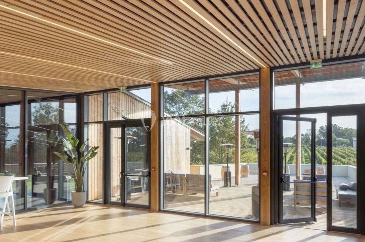 Intérieur lumineux avec parquet en bois, plafond à lattes, grandes baies vitrées et vue sur une terrasse et la végétation.