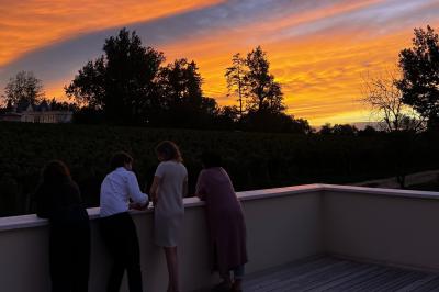 Quatre personnes regardent un coucher de soleil aux teintes orange et violet depuis une terrasse surplombant des vignes.
