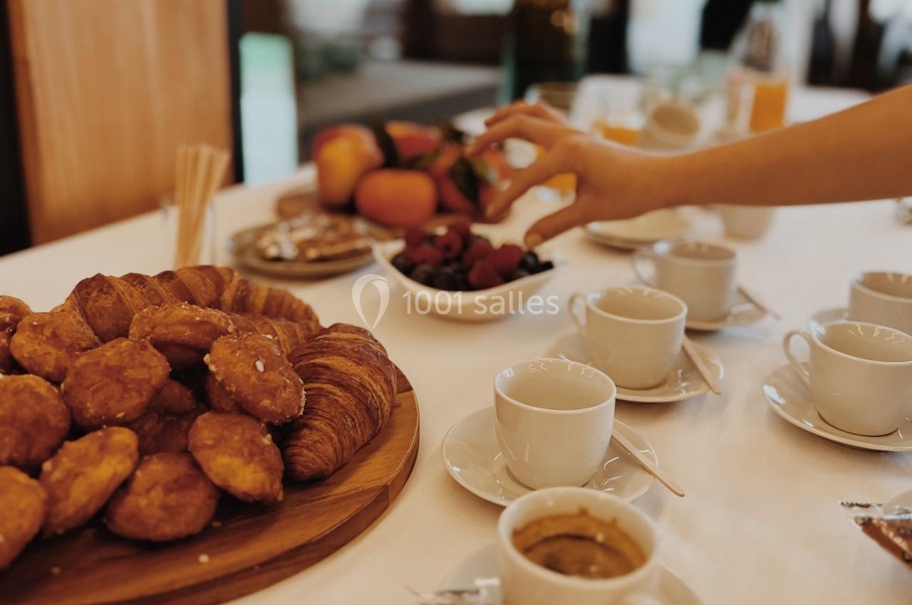 Table dressée pour un petit-déjeuner avec viennoiseries, fruits, café et une main prenant des cerises.