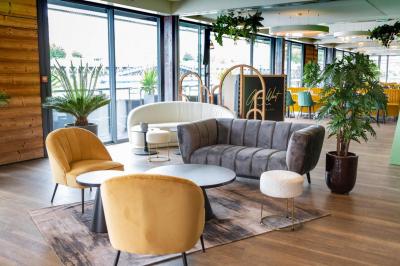 Terrasse avec tables, chaises et plantes, donnant sur une rivière bordée de bâtiments et d'un pont au loin.