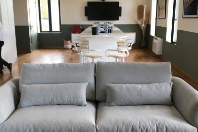 Façade d'un bâtiment clair avec une terrasse aménagée, un grand arbre et un ciel bleu en arrière-plan.