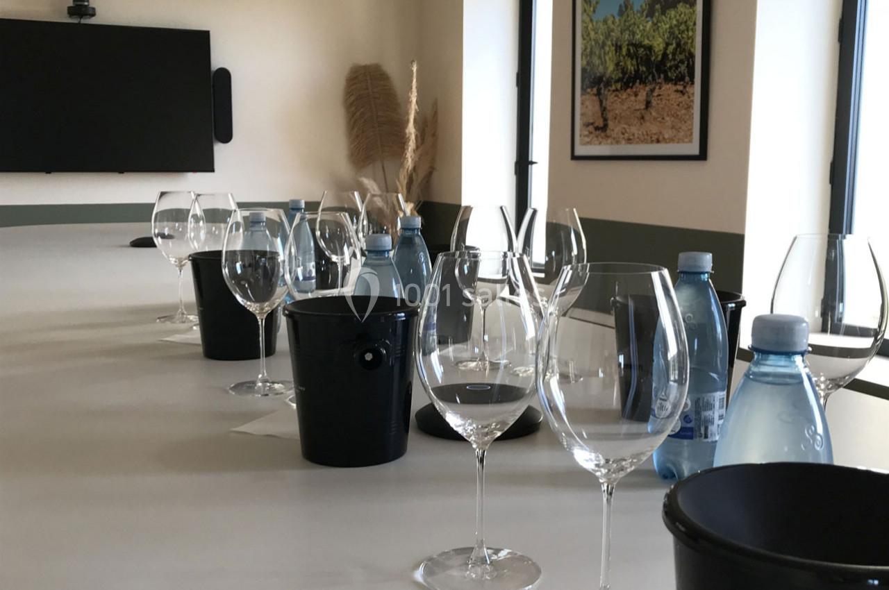 Table dressée avec des verres à vin, seaux noirs et bouteilles d'eau dans une salle lumineuse décorée sobrement.