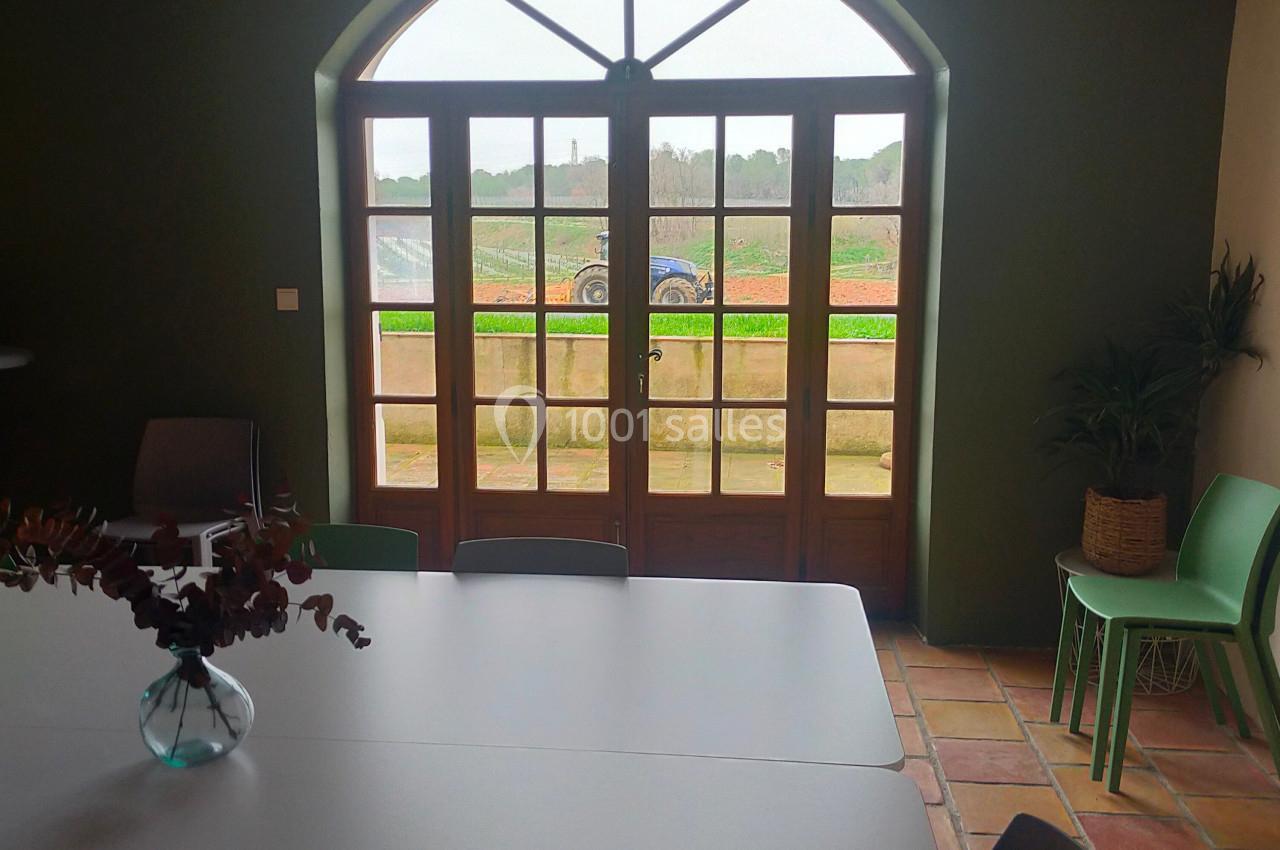 Grande baie vitrée en arche donnant sur un paysage champêtre, vue depuis une salle avec table et chaises.