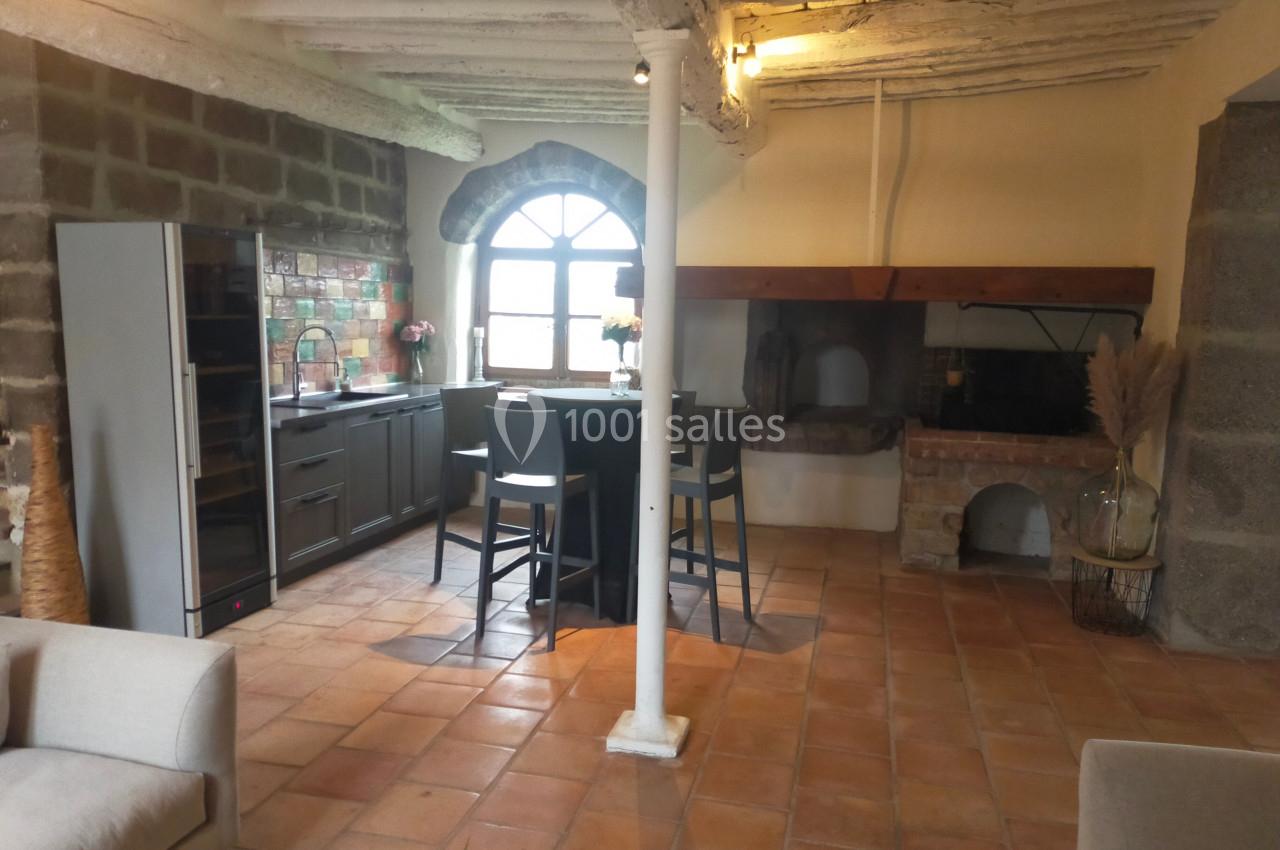 Cuisine rustique avec poutres apparentes, sol en terre cuite, îlot central, four à bois et fenêtre en arche.