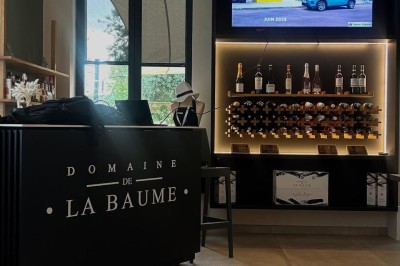 Salle lumineuse avec un long comptoir blanc, des tabourets, des bouteilles exposées et des poutres apparentes au plafond.