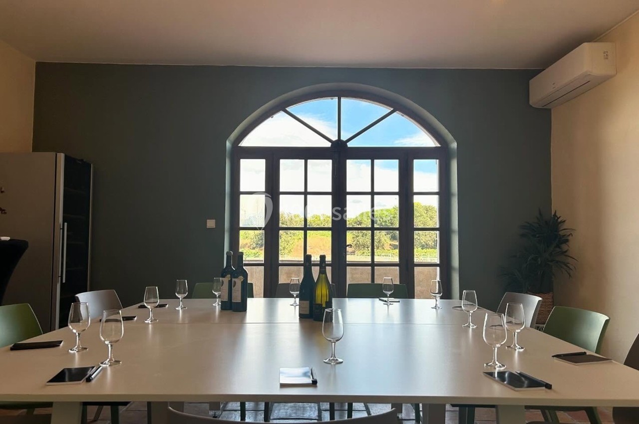 Salle de réunion lumineuse avec une table blanche, des verres, des bouteilles de vin et une grande fenêtre donnant sur l…