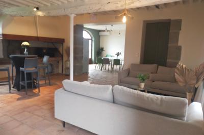 Façade d'un bâtiment clair avec une terrasse aménagée, un grand arbre et un ciel bleu en arrière-plan.