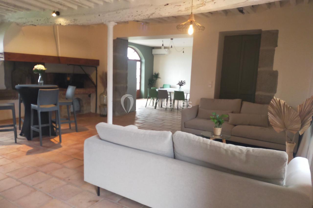 Salon lumineux avec canapés gris, table haute près d'une cheminée et vue sur une salle à manger en arrière-plan.