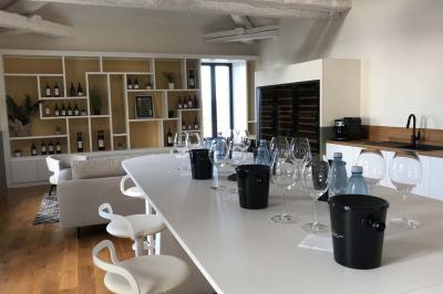 Façade d'un bâtiment clair avec une terrasse aménagée, un grand arbre et un ciel bleu en arrière-plan.