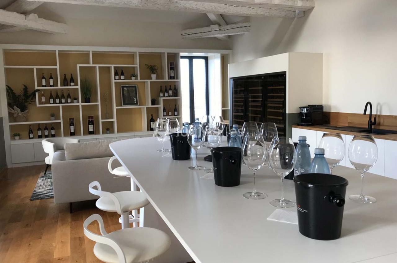 Salle lumineuse avec un comptoir équipé de verres à vin, crachoirs et bouteilles, entourée d'étagères et d'un canapé.