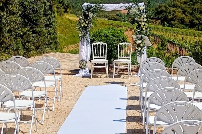 Allée décorée pour une cérémonie en plein air avec chaises en paille, arche florale et paysage boisé en arrière-plan.