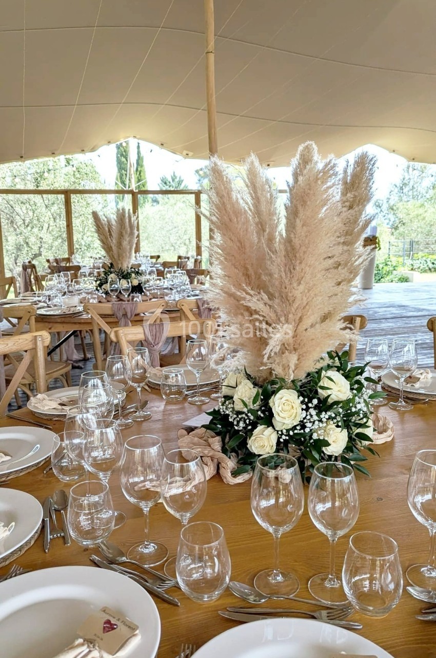 Table de réception décorée avec des fleurs blanches, des herbes de la pampa et une vaisselle élégante sous une tente.