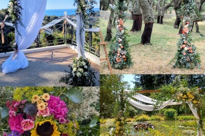 Allée décorée pour une cérémonie en plein air avec chaises en paille, arche florale et paysage boisé en arrière-plan.