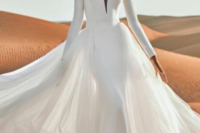 Femme portant une robe de mariée blanche avec un dos ouvert, posant dans un jardin fleuri.