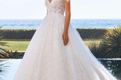 Femme portant une robe de mariée blanche avec un dos ouvert, posant dans un jardin fleuri.