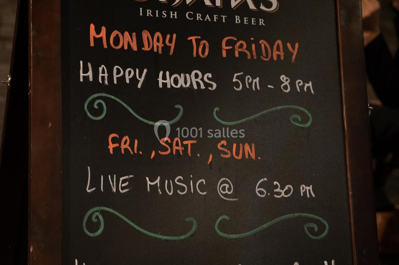 Tableau noir annonçant les horaires des happy hours, musique live et disponibilité de la cuisine dans un bar.