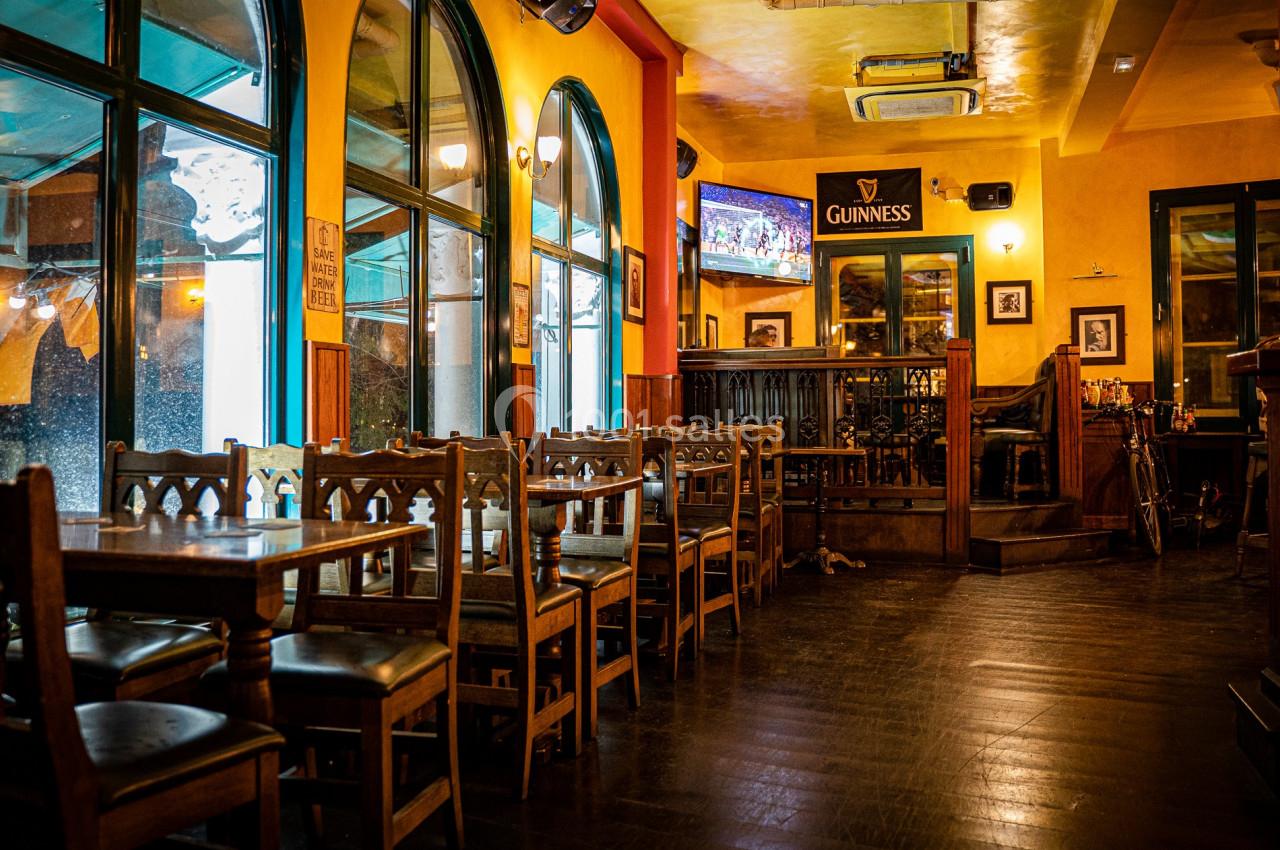 Intérieur d'un pub chaleureux avec des tables en bois, des chaises alignées et un bar en arrière-plan.