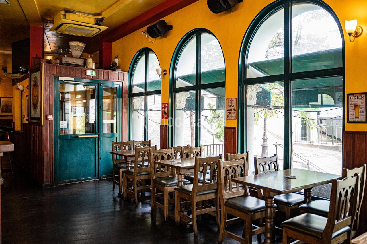 Salle de restaurant vide avec des tables en bois, des chaises sculptées et de grandes fenêtres en arche donnant sur l…