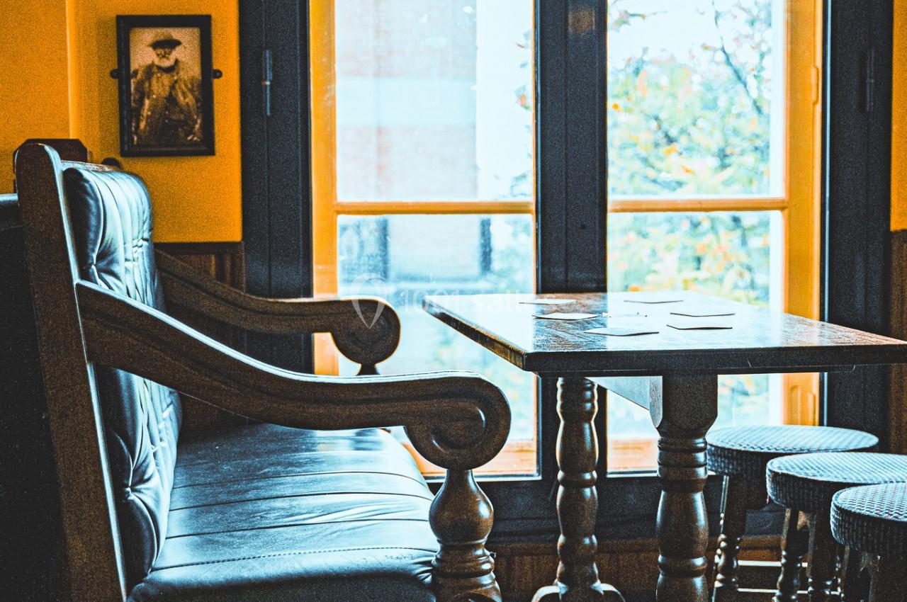 Intérieur d'un café avec une table en bois, des chaises et un banc près d'une fenêtre laissant entrer la lumière.